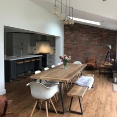 a dining room table with white chairs and wooden benches in front of an open kitchen