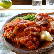 a wooden bowl filled with mashed potatoes, peas and meat sauce on top of a table