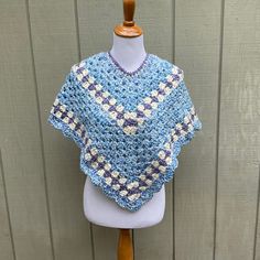 a blue and white crocheted shawl sitting on top of a mannequin