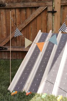 a toy car race track set up in the grass next to a wooden fence with bunting flags