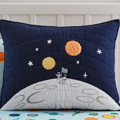 a pillow with an astronaut on the moon and stars in the sky, sitting on top of a bed