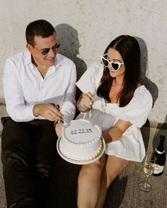 a man and woman sitting next to each other holding a cake