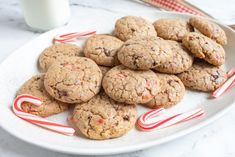 chocolate chip cookies and candy canes on a white plate next to a glass of milk