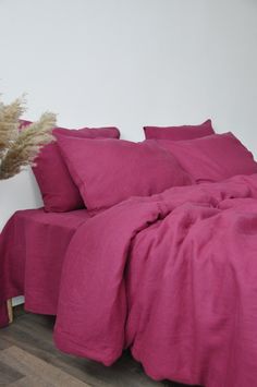 a bed with pink sheets and pillows on top of it next to a plant in a white vase