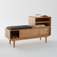 a small wooden cabinet with a black cushion on it's seat and an open book shelf