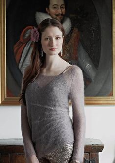 a woman standing in front of a painting wearing gold sequin shorts and a gray sweater