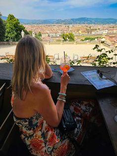 a woman sitting at a table with a drink in her hand and looking out over the city