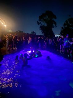 people are in the pool at night with blue lights and water around them, while others look on