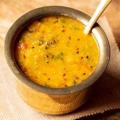 a small metal bowl filled with soup on top of a cloth covered table next to a wooden spoon