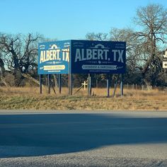 two blue billboards sitting on the side of a road in front of some trees