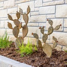 three metal cactus sculptures in front of a brick wall and green grass on the ground