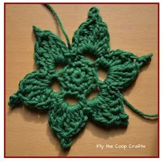 a green crocheted flower on top of a wooden table