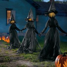 three halloween witches walking in front of a house with pumpkins on the ground and one holding hands