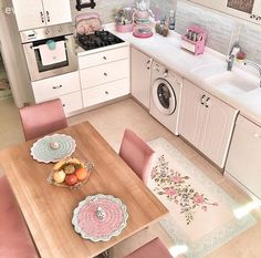 a kitchen filled with lots of white appliances and wooden table surrounded by pink dining chairs