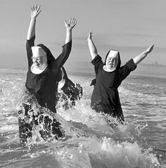 black and white photograph of two women in the ocean with their arms up, both wearing nun costumes