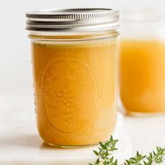 a glass jar filled with orange liquid next to some green leaves