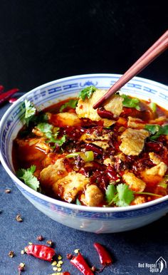 a blue and white bowl filled with food next to some red chili peppers on the side