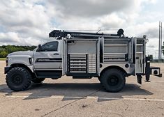 a large truck parked in a parking lot next to a field with trees and clouds