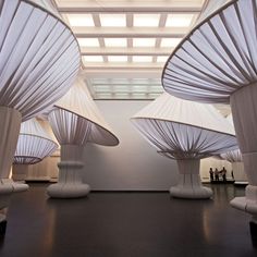 several white sculptures are on display in a room with wood flooring and ceiling lights