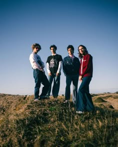 four young men standing on top of a grass covered hill with blue skies in the background