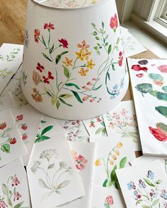 many cards are laid out on the floor next to a lamp shade with flowers painted on them