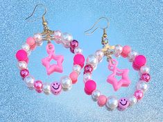 These earrings feature wire hoops adorned with pink and white faux pearls, matte pink beads and pink happy face beads with pink plastic stars in the center. The ear wires are nickel-free brass. If you are interested in these earrings and have an allergy or sensitivity and require a different type of ear wire, feel free to contact me and I will try my best to accommodate you! These  earrings measure 6cm (2.5") in total length, and the rings are 4.5cm (1.75") in width at the widest point. All find Trendy Pink Beaded Earrings With Round Beads, Trendy Pink Beaded Earrings, Trendy Pink Hoop Earrings With Round Beads, Handmade Pink Trendy Beaded Earrings, Whimsical Pink Beaded Earrings, Trendy Handmade Pink Beaded Earrings, Pink Star Charm Dangle Earrings, Pink Dangle Earrings With Star Charm, Pink Star Earrings For Party