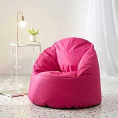 a bright pink bean bag chair next to a white table with a laptop on it