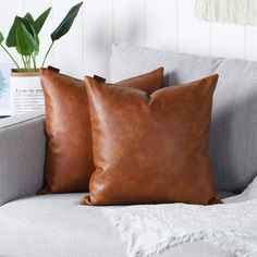 two brown pillows sitting on top of a gray couch next to a potted plant