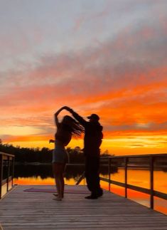 two people standing on a dock at sunset