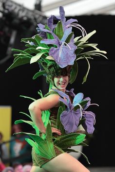 a woman in green and purple costume walking down the runway with flowers on her head