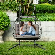 two women sitting in a swing chair with pillows on the back and one woman talking to each other