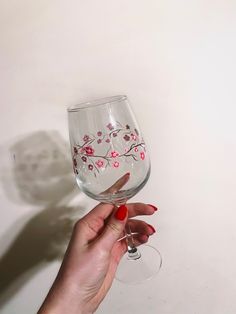 a hand holding a wine glass with pink flowers painted on the bottom and red nail polish