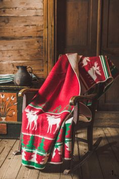 an old rocking chair covered with a red and green christmas blanket in front of a wooden wall