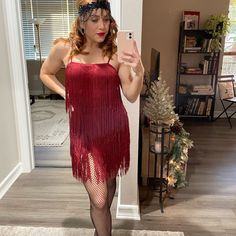 a woman in a red fringe dress taking a selfie with her cell phone while wearing fishnet stockings