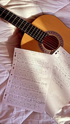 a guitar sitting on top of a bed next to sheets of paper with musical notes