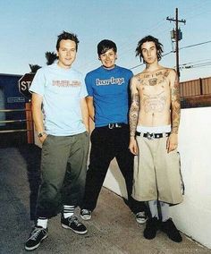 three men standing next to each other near a wall with tattoos on their arms and chest