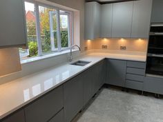 an empty kitchen with white counter tops and gray cupboards on either side of the window