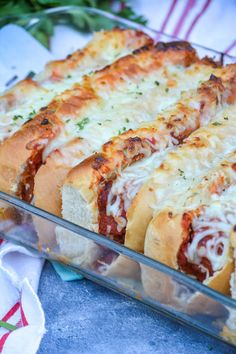 four hotdogs with cheese and sauce in a glass casserole dish on a table