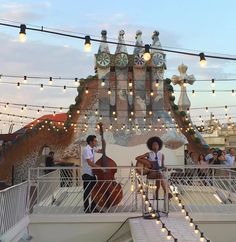 two people on a balcony with string lights strung across the ceiling and an elaborately decorated building in the background