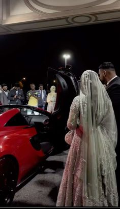 a man and woman standing next to a red sports car