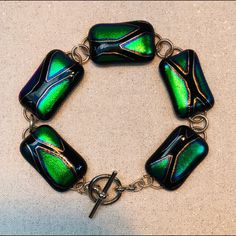 a green and black bracelet with metal clasps on a white tablecloth background,