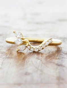 a yellow gold ring with two pear shaped diamonds on the top and bottom, sitting on a piece of wood