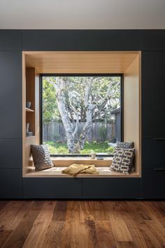 a window seat in the corner of a room with wooden floors and black walls, overlooking a tree