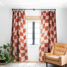 an orange and white checkered curtain hangs in front of a window with a chair next to it