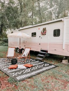 an rv is parked in the grass with two chairs and an umbrella on top of it