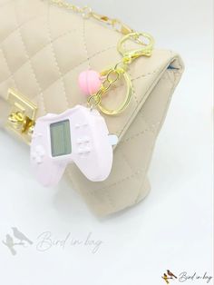 a pink game controller keychain sitting on top of a beige purse with a gold chain