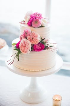 a three tiered cake with pink flowers and greenery sits on a white table