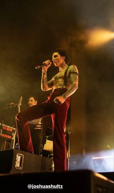 a man standing on top of a stage holding a microphone in front of him and wearing red pants