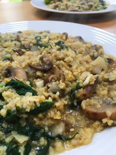 a white plate topped with rice covered in mushroom and spinach topping next to another plate filled with vegetables