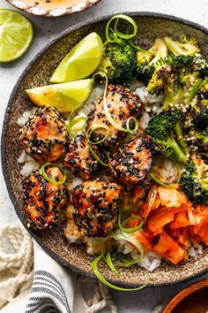 a bowl filled with rice, broccoli and carrots next to lime wedges